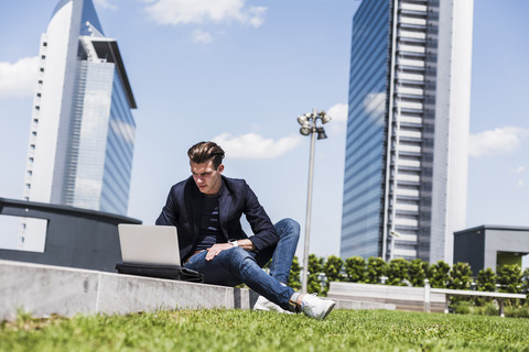 Junger Mann sitzt im Freien und benutzt einen Laptop, lizenzfreies Stockfoto