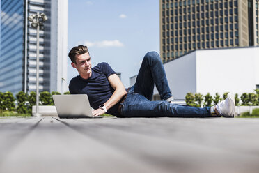 Junger Mann liegt im Freien und benutzt einen Laptop - UUF007552