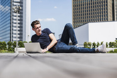 Young man lying outdoors using laptop - UUF007552