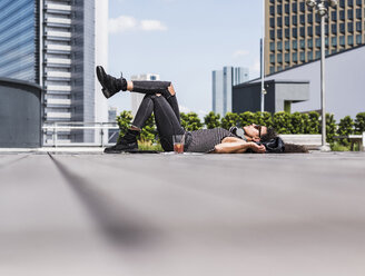 Relaxed young woman wearing headphones lying on the ground - UUF007553