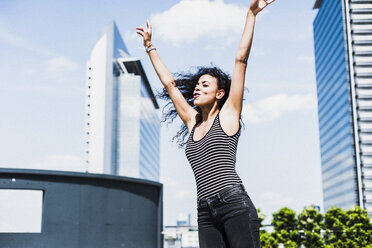 Enthusiastic young woman raising her arms outdoors - UUF007558