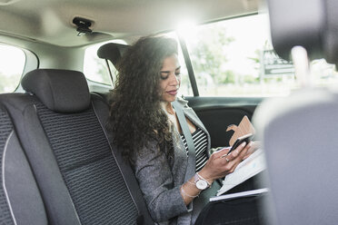 Junge Frau im Auto schaut auf ihr Handy - UUF007564