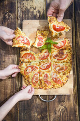 Hands taking pieces of homemade pizza with cauliflower and tomatoes - SARF002729