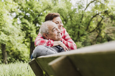 Glückliche Frau, die ihren alten Vater umarmt, der auf einer Bank in der Natur sitzt - UUF007569