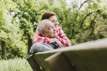 Happy woman hugging her old father sitting on a bench in nature - UUF007569