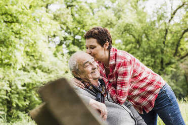 Glückliche Frau küsst ihren alten Vater auf einer Bank in der Natur sitzend - UUF007571