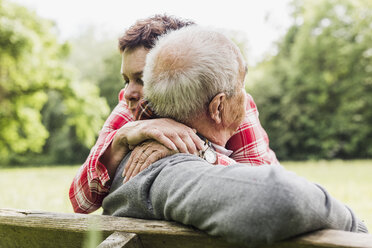 Happy woman hugging her old father sitting on a bench in nature - UUF007573