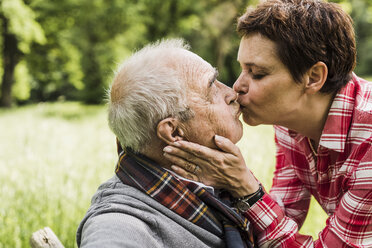 Frau küsst ihren alten Vater auf einer Bank in der Natur sitzend - UUF007575
