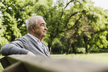 Lächelnder älterer Mann sitzt auf einer Bank in der Natur - UUF007576
