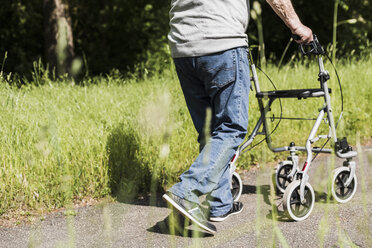 Rückenansicht eines älteren Mannes, der mit einer Gehhilfe auf Rädern in der Natur spazieren geht - UUF007584