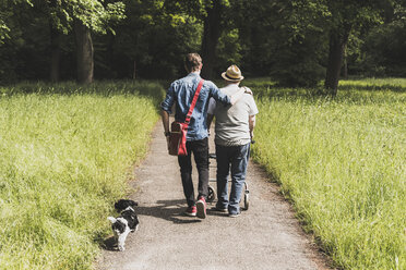 Rückenansicht des Großvaters, der mit Enkel und Hund in der Natur spazieren geht - UUF007589