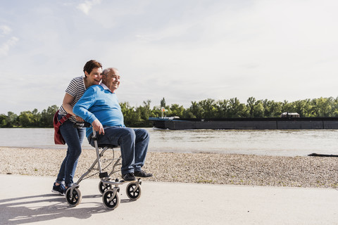 Frau schiebt ihren alten Vater, der auf einer Gehhilfe auf Rädern sitzt, lizenzfreies Stockfoto