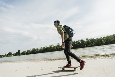 Skateboard fahrender junger Mann mit Kopfhörern - UUF007637