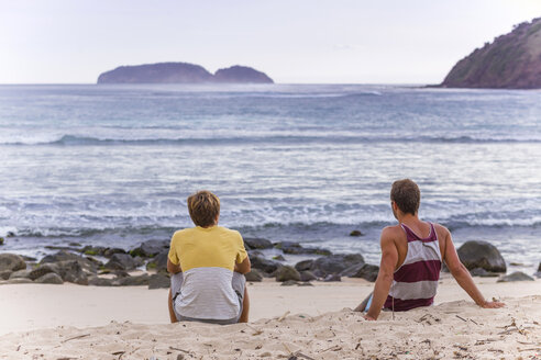 Indonesien, Insel Sumbawa, Zwei junge Männer sitzen am Strand - KNTF000304