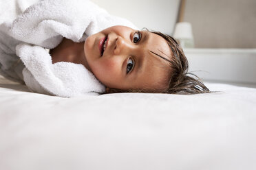Portrait of little boy with shower towel lying on the bed after taking a bath - VABF000516