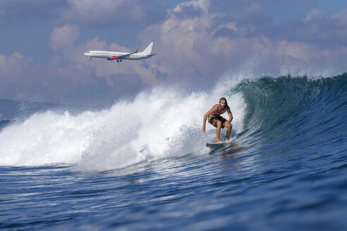 Indonesia, Bali, Surfer on wave, airplane in the background - KNTF000320