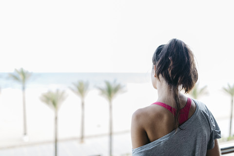 Junge Frau auf Balkon mit Blick auf Palmenstrand, lizenzfreies Stockfoto