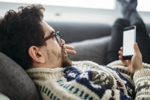 Mann liegt auf einer Couch und schaut auf sein Smartphone - LCUF000020