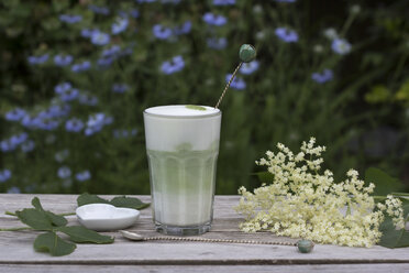 Matcha Tee mit Milch im Glas auf Holz, Holunderblüten und herzförmigem Porzellan mit Löffel - YFF000546