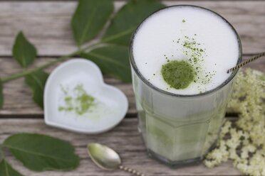 Matcha tea with milk in glass on wood, elderflowers and heart shaped porcellain bowl - YFF000548