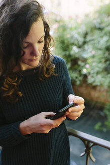 Junge Frau steht auf einem Balkon und benutzt ein Smartphone - BOYF000378