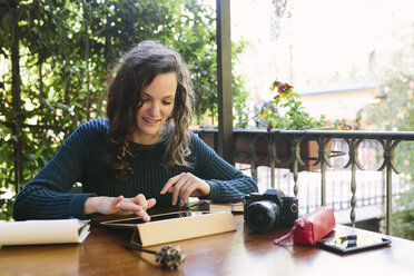 Junge Frau sitzt auf einem Balkon und arbeitet mit einem digitalen Tablet - BOYF000379