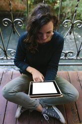 Junge Frau sitzt auf einem Balkon und arbeitet mit einem digitalen Tablet - BOYF000385