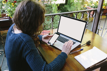 Young woman sitting on balcony using laptop and smart phone - BOYF000389