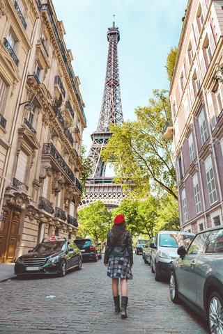 Frankreich, Paris, Eiffelturm zwischen den Gebäuden, Straße in der Nähe und Frau mit roter Baskenmütze auf der Straße, lizenzfreies Stockfoto