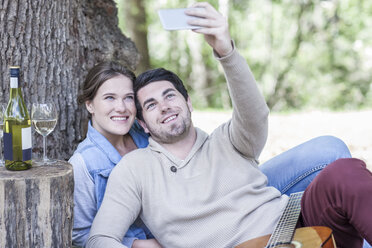 Lächelndes junges Paar bei einem Picknick mit Weißwein und einem Selfie - ZEF008677