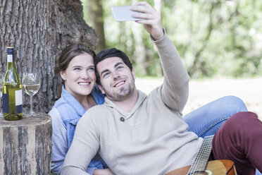 Smiling young couple having a picnic with white wine taking a selfie - ZEF008677