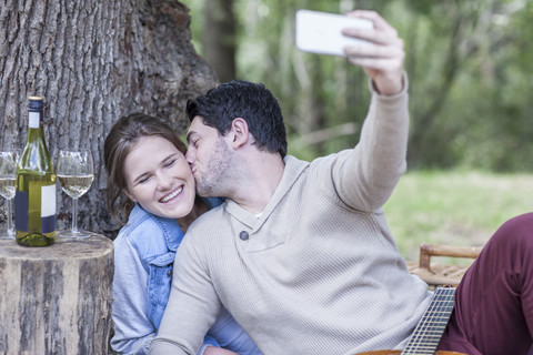 Glückliches junges Paar bei einem Picknick mit Weißwein und einem Selfie, lizenzfreies Stockfoto