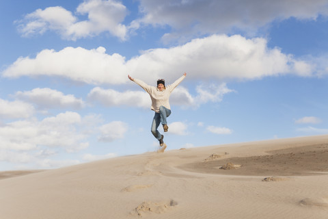 Enthusiastische reife Frau springt über Sanddüne, lizenzfreies Stockfoto