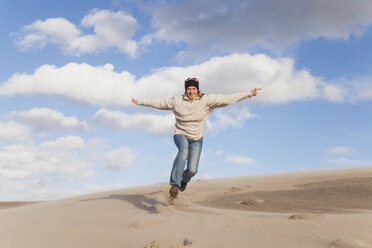 Enthusiastic mature woman running and jumping on sand dune - GWF004736