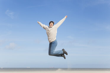 Enthusiastic mature woman jumping on beach - GWF004737