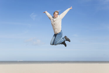 Enthusiastic mature woman jumping on beach - GWF004738