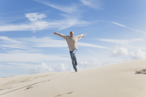 Enthusiastische reife Frau läuft entlang einer Sanddüne, lizenzfreies Stockfoto