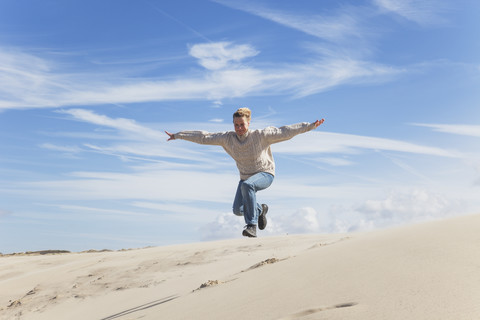 Enthusiastische reife Frau springt über Sanddüne, lizenzfreies Stockfoto