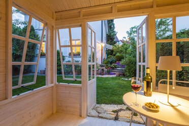 Red wine glass and bottle and bowl of olives on table in a garden shed - WDF003606