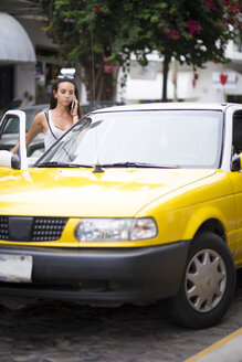 Junge Frau am Telefon beim Einsteigen in ein Taxi - ABAF002047