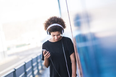 Young woman with headphones and smartphone leaning against wall - SIPF000540