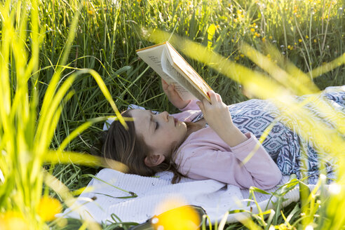 Kleines Mädchen liegt auf einem Blumenfeld und liest ein Buch - SARF002743