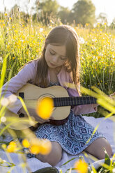 Porträt eines kleinen Mädchens, das auf einem Blumenfeld Gitarre spielt - SARF002744