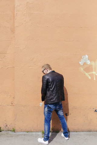 Rückansicht eines jungen Mannes, der an die Fassade pinkelt, lizenzfreies Stockfoto