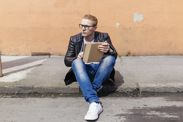 Junger Mann mit digitalem Tablet am Bordstein sitzend - BOYF000410