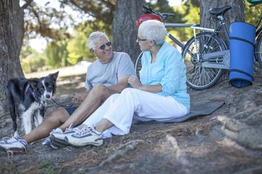 Elderly couple sitting outdoors with dog and bicycles - ZEF008704