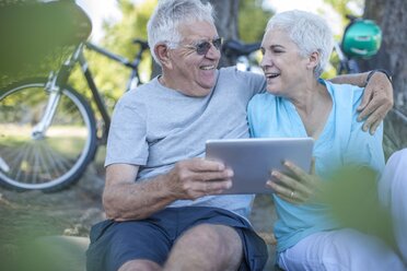 Happy elderly couple sitting outdoors with digital tablet - ZEF008708