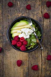 Bowl of avocado raspberry salad with feta on dark wood - LVF004946