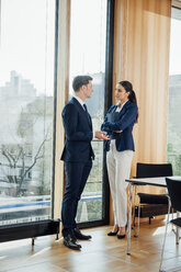 Businessman and businesswoman in office talking at the window - CHAF001770