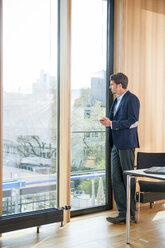 Geschäftsmann im Büro schaut aus dem Fenster - CHAF001771